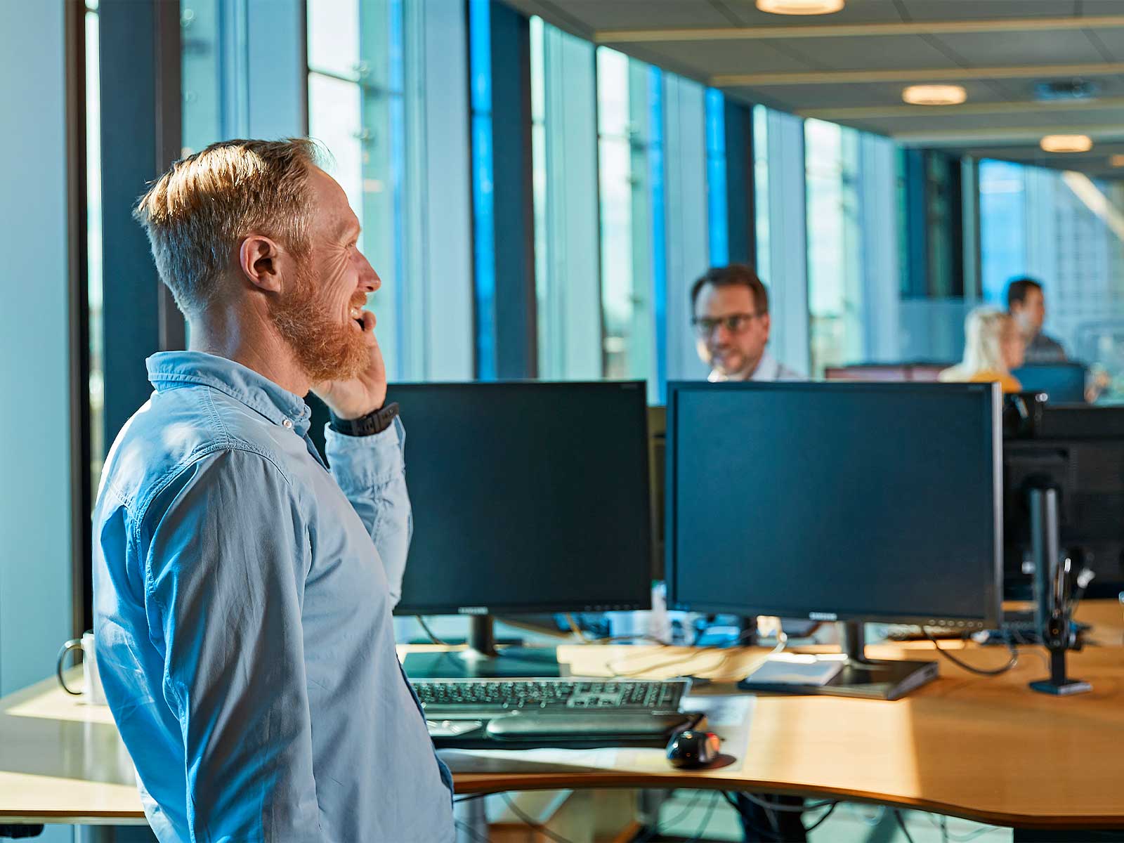 Kontormiljø med to mænd der sidder ved borde med computerskærme. Karriere hos EWII Fibernet.